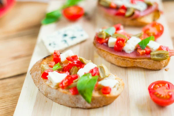 Bruschetta tradicional italiana con queso azul, feta, tomates, hojas de albahaca, jamón sobre un fondo de madera . —  Fotos de Stock