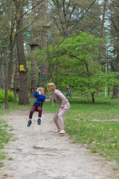 A mãe enrola o filho no teleférico. Atividades de lazer no parque. Interação mútua entre mãe e filho . — Fotografia de Stock