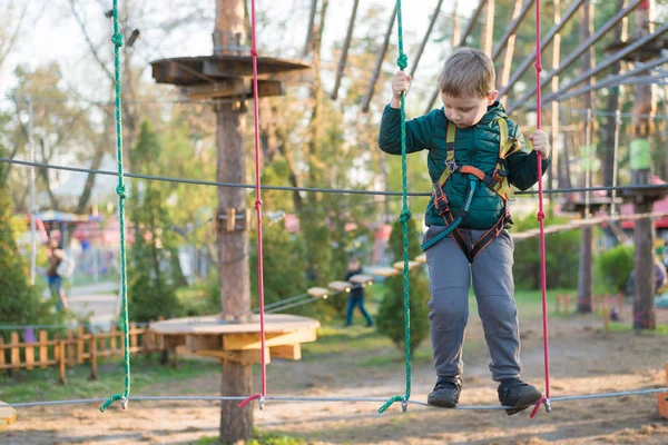 Kleine jongen in een touwenpark. Actieve fysieke recreatie van het kind in de frisse lucht in het park. Opleiding voor kinderen. — Stockfoto