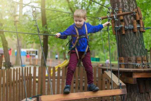 Un niño pequeño está entrenando en un parque de cuerdas. El niño sube la carrera de obstáculos. Recreación activa en el parque al aire libre . — Foto de Stock