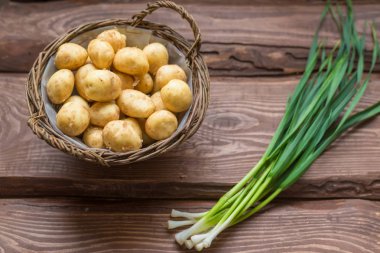 Ahşap bir arka plan üzerinde çiğ taze organik patates ve yeşil soğan.