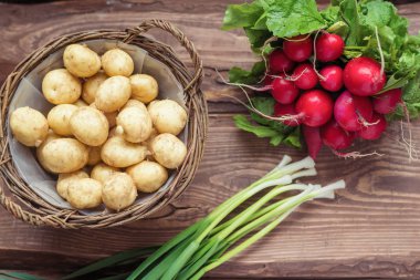 Taze çiğ organik sebzeler: patates, turp, ahşap bir arka plan üzerinde yeşil soğan.