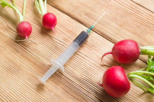 GMO concept in vegetables. The hand makes a shot with a syringe in a radish to increase the volume.