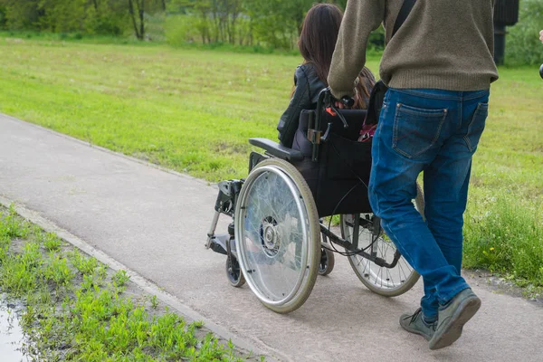 Мужчина несет женщину в инвалидном кресле по дороге . — стоковое фото