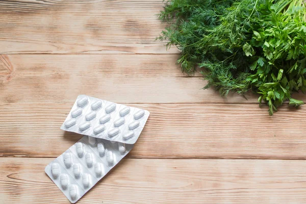 The concept of natural medicine, vitamins. Fresh dill and pills on wooden background. Treatment with a healthy diet.