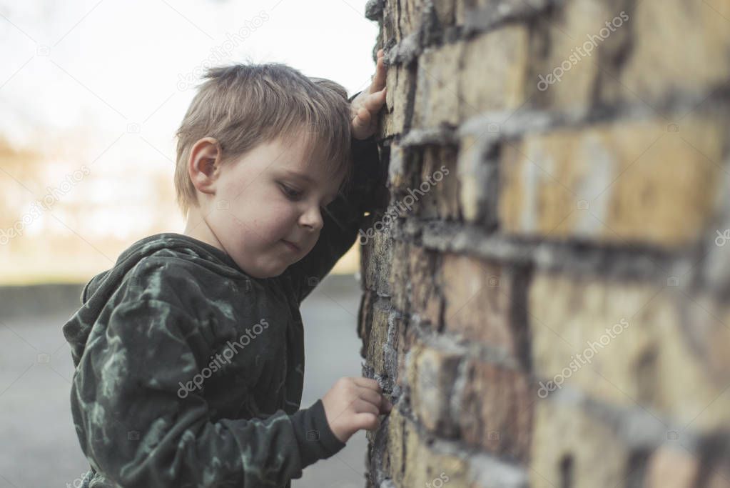Child confused, depressed, upset. Little boy near the brick destroyed wall.