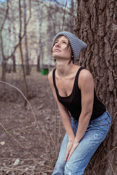 A young woman wearing a jersey and hat is standing near a tree. The concept of outdoor recreation, hiking.