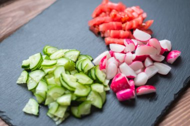 Dilimlenmiş taze salatalık, domates ve siyah bir arka plan üzerinde kırmızı turp. Sebzeden salata pişirmek. Sağlıklı beslenme kavramı, vejetaryenlik.