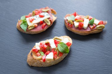 Mavi peynir, beyaz peynir, domates, fesleğen yaprakları, siyah taş arka plan üzerinde jamon ile Geleneksel İtalyan bruschetta.