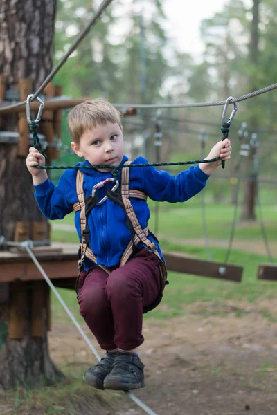 Malý chlapec cvič v lanové parku. Dítě šplhá po překážkách. Aktivní rekreace v parku v čerstvém vzduchu. — Stock fotografie