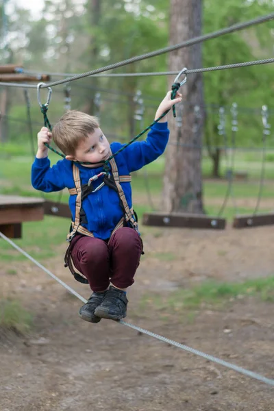 Malý chlapec cvič v lanové parku. Dítě šplhá po překážkách. Aktivní rekreace v parku v čerstvém vzduchu. — Stock fotografie