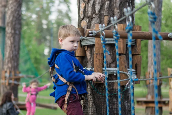 Een kleine jongen is trainen in een touw park. Het kind klimt de hindernisbaan. Actieve recreatie in het Park in de frisse lucht. — Stockfoto