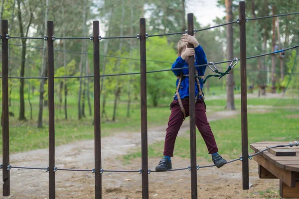 En liten pojke tränar i en reppark. Barnet klättrar på hinderbanan. Aktiv rekreation i parken i friska luften. — Stockfoto