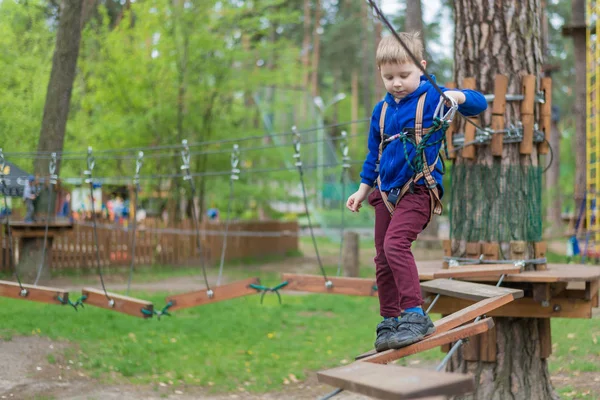 Мальчик тренируется в веревочном парке. Ребенок поднимается на полосу препятствий. Активный отдых в парке на свежем воздухе . — стоковое фото