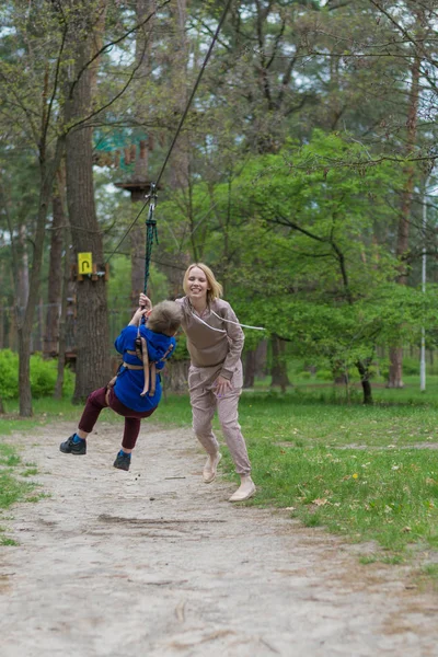 A mãe enrola o filho no teleférico. Atividades de lazer no parque. Interação mútua entre mãe e filho . — Fotografia de Stock
