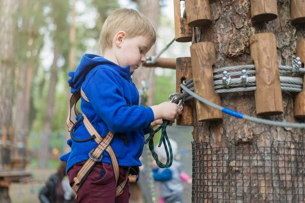 Een kleine jongen is trainen in een touw park. Het kind klimt de hindernisbaan. Actieve recreatie in het Park in de frisse lucht. — Stockfoto