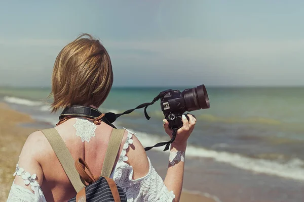 Ženská fotografka na moři. Na pobřeží vede žena středního věku v bílých šatech s kamerou. Letní turistika, fotografování atrakcí na dovolené. — Stock fotografie