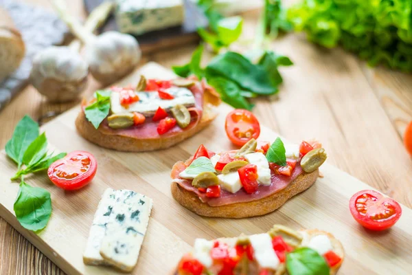 Bruschetta tradicional italiana con queso azul, feta, tomates, hojas de albahaca, jamón sobre un fondo de madera . —  Fotos de Stock