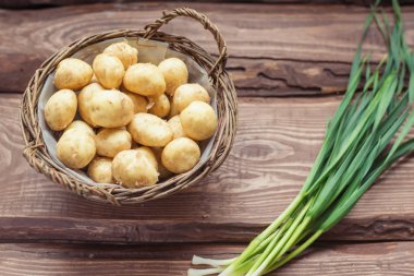 Ahşap bir arka plan üzerinde çiğ taze organik patates ve yeşil soğan.