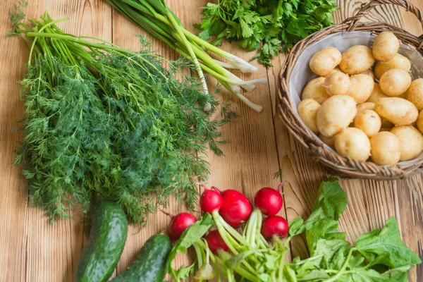 Świeże surowe warzywa organiczne: ziemniaki, rzodkiewki, zielone cebulki, ogórki na drewnianym tle. — Zdjęcie stockowe