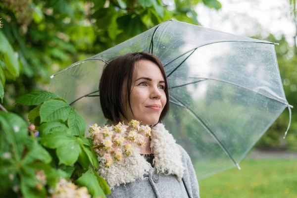 Vrouw onder een paraplu in de regen bij een kastanjeboom. — Stockfoto