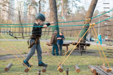 Küçük bir çocuk engelli parkurdan geçiyor. Parkta temiz havada çocuğun aktif fiziksel rekreasyon. Çocuklar için eğitim.