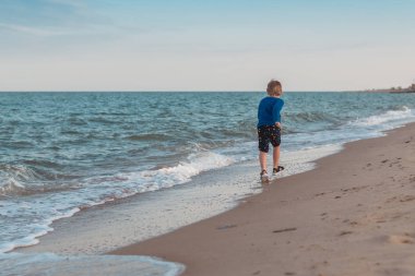 Küçük bir çocuk deniz kıyılarında, okyanus boyunca koşuyor. Yaz aylarında boş zaman aktiviteleri.