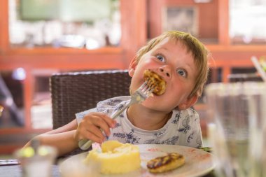 5-6 yaşlarında küçük bir çocuk bir restoranda patates püresi ve pirzama yiyor..