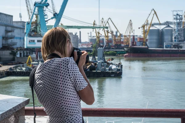 A woman photographs the ships in the seaport.