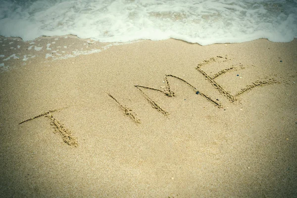 Il tempo è il concetto ultimo. La parola Tempo scritto nella sabbia e scomparire sotto l'influenza dell'onda del mare . Foto Stock Royalty Free