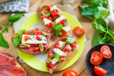 Mavi peynir, beyaz peynir, domates, fesleğen yaprakları, ahşap bir arka plan üzerinde jamon ile Geleneksel İtalyan bruschetta.