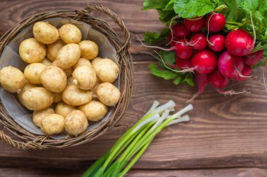 Taze çiğ organik sebzeler: patates, turp, ahşap bir arka plan üzerinde yeşil soğan.
