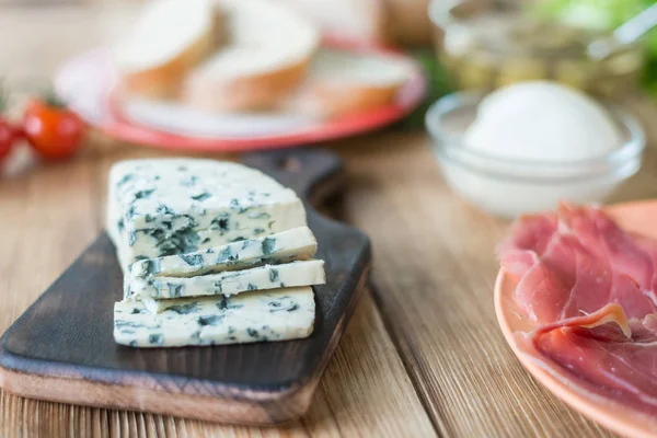 Sliced blue cheese on a wooden background and different products. Preparation for cooking snacks.