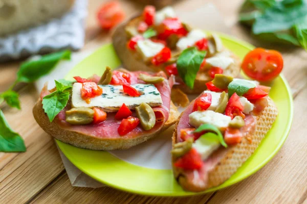 Bruschetta tradicional italiana con queso azul, feta, tomates, hojas de albahaca, jamón sobre un fondo de madera . —  Fotos de Stock