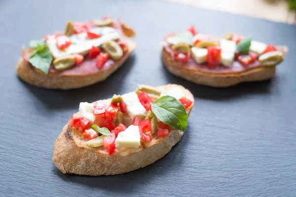 Traditional Italian bruschetta with blue cheese, feta, tomatoes, basil leaves, jamon on black stone background. — Stock Photo, Image