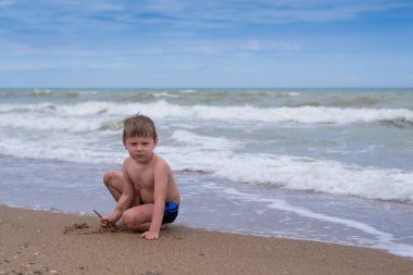 Küçük bir çocuk deniz kenarında suyun yanında oynuyor..