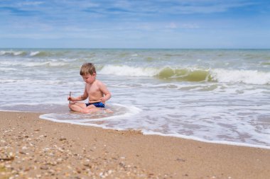 Küçük bir çocuk deniz kenarında suyun yanında oynuyor..
