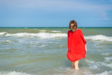 Kırmızı elbiseli bir kadın denize suda yürüyor..