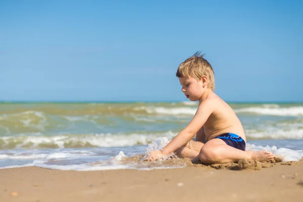 Malý chlapec s nespokojený, uražený pohled sedí ve vodě u moře. — Stock fotografie