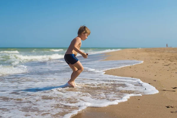 Маленький мальчик с недовольным, оскорбленным видом сидит в воде у моря . — стоковое фото
