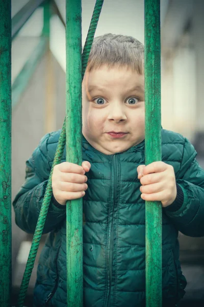 El niño está tras las rejas. Un niño está detrás de una valla de metal . — Foto de Stock