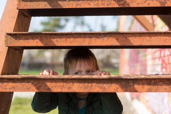 Bir çocuğun yalnızlığı. Küçük bir çocuk eski metal basamakların arkasından dışarı bakar.. — Stok fotoğraf