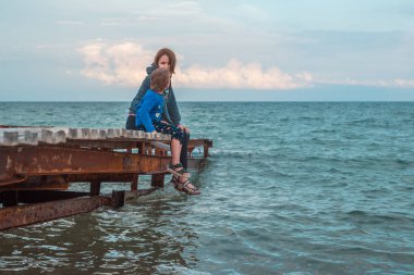Annem ve küçük oğlu denizdeki iskelede, okyanusta birlikte oturuyorlar. Etkileşim, iletişim anne ve çocuk.
