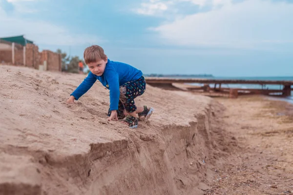 Маленький мальчик забирается на песок у моря, океана . — стоковое фото