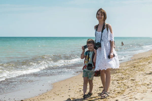 Máma a syn s kamerami na pláži, oceán. Společná okupace matky a dítěte, aby fotografoval. Interakce v rodině, společné zájmy. — Stock fotografie