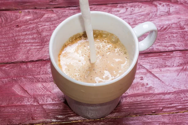 Молоко вливають у чашку кави на дерев'яному фоні бордового кольору . — стокове фото