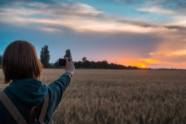 Женщина фотографирует закат на пшеничном поле . — стоковое фото