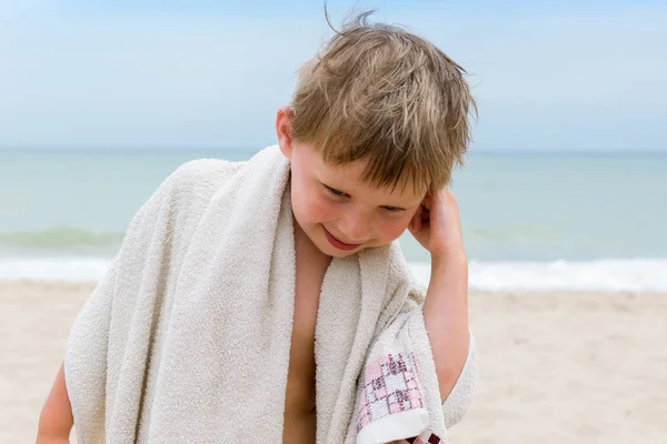 Malý chlapec si utírá mokrou hlavu s ručníkem na moři. — Stock fotografie