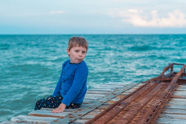 एक छोटा लड़का समुद्र में बंदरगाह पर बैठा है . — स्टॉक फ़ोटो, इमेज