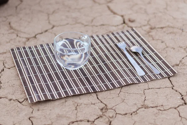 A cup of water and cutlery on the dried ground. The concept of water, as the most necessary for human survival.